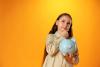 Smiling little girl posing with a piggy bank over yellow background
