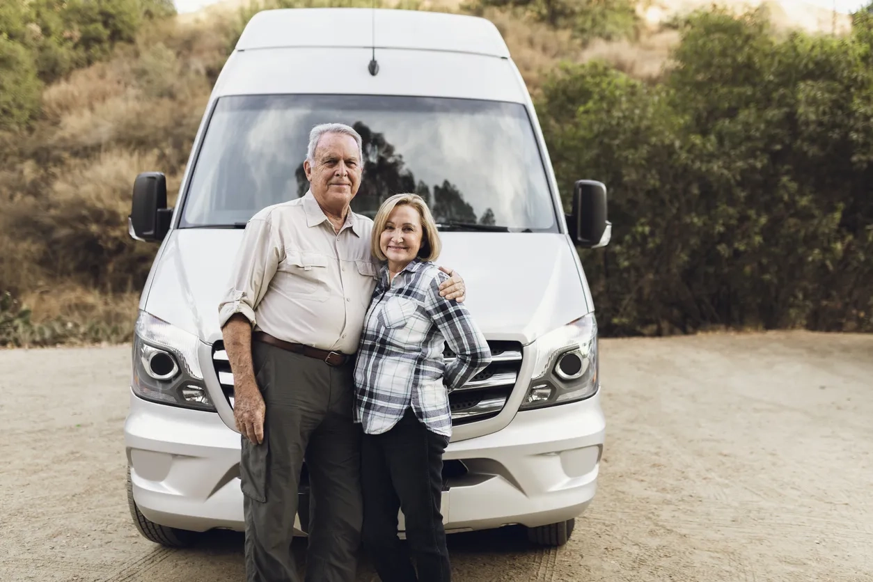 Senior couple smiling stood in front of a camper van