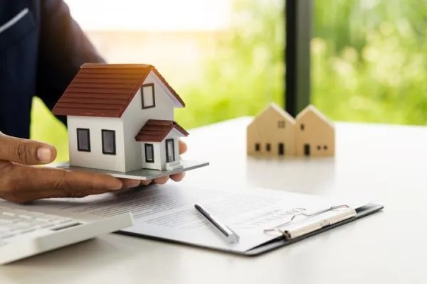 man holding a small model house above a printed document