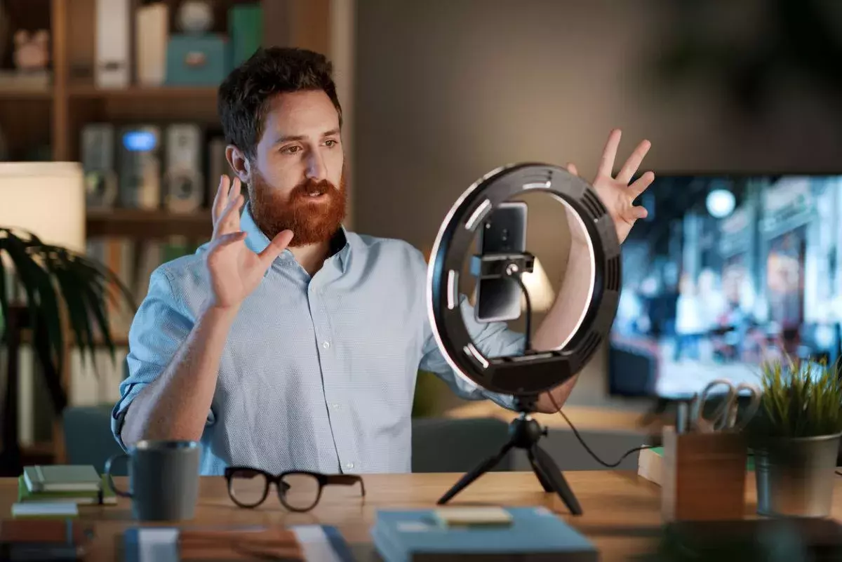 Professional youtuber and influencer working at home, he is recording a new video using a smartphone and a ring light