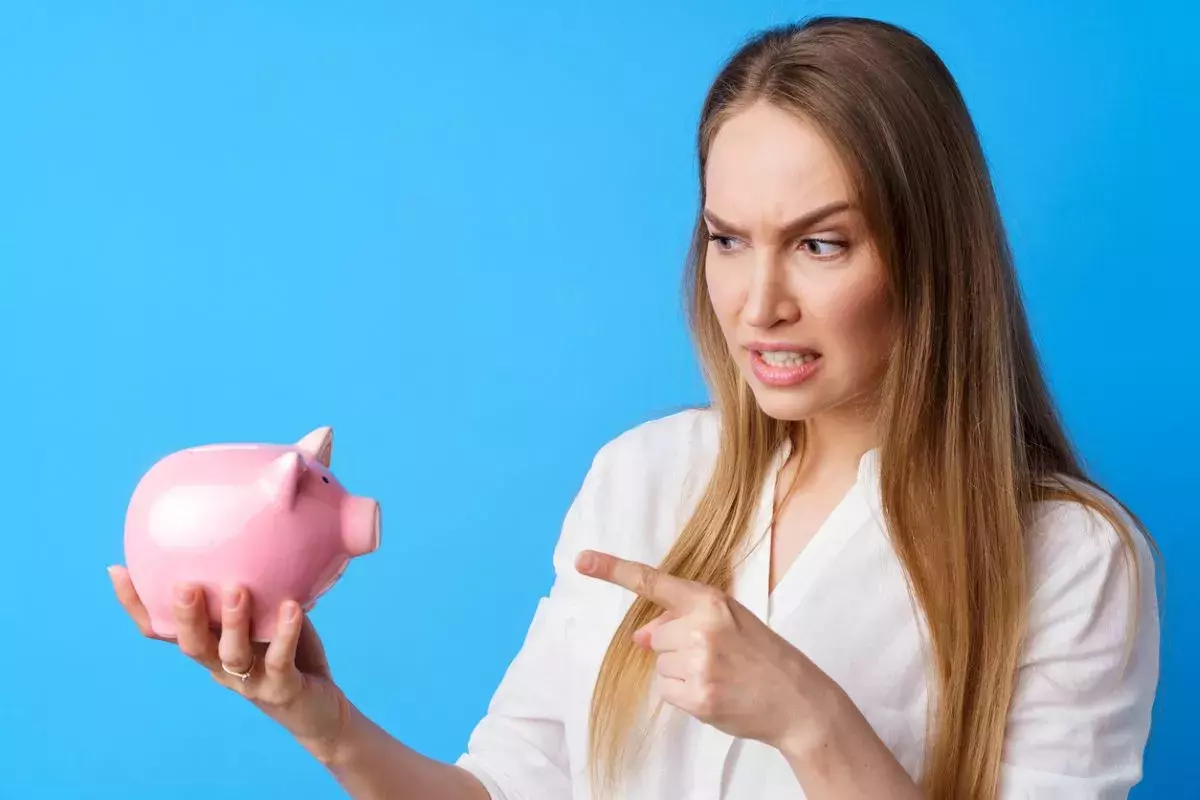 Unhappy woman holding piggy bank moneybox against blue background