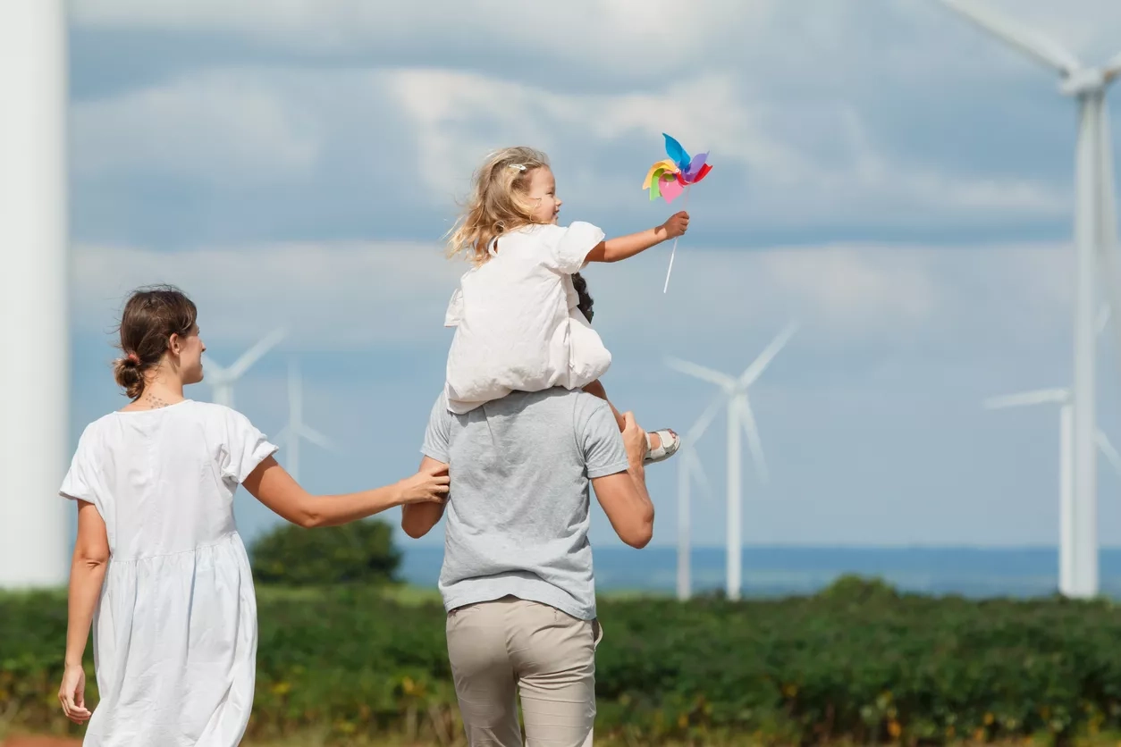 Family teaching young child about renewable energy and sustainability near wind turbines.