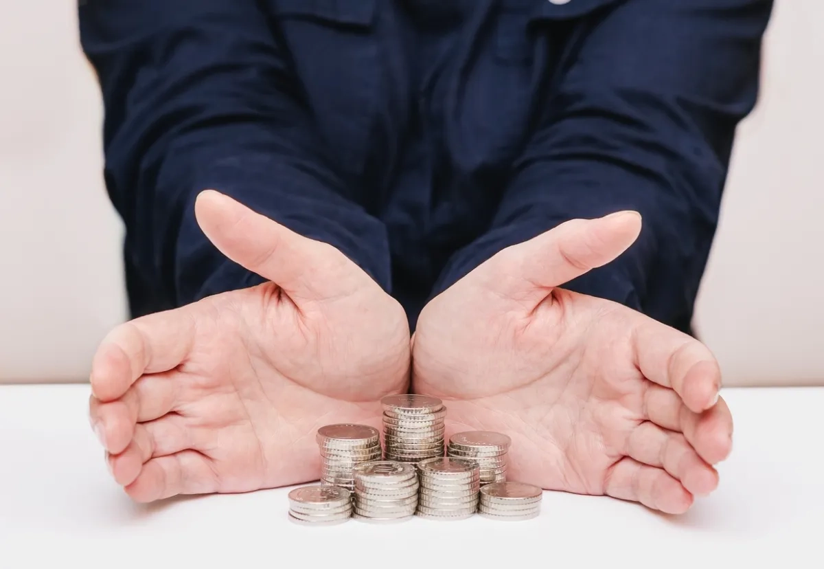 Woman palms are open, protecting money coins are stacked in stacks