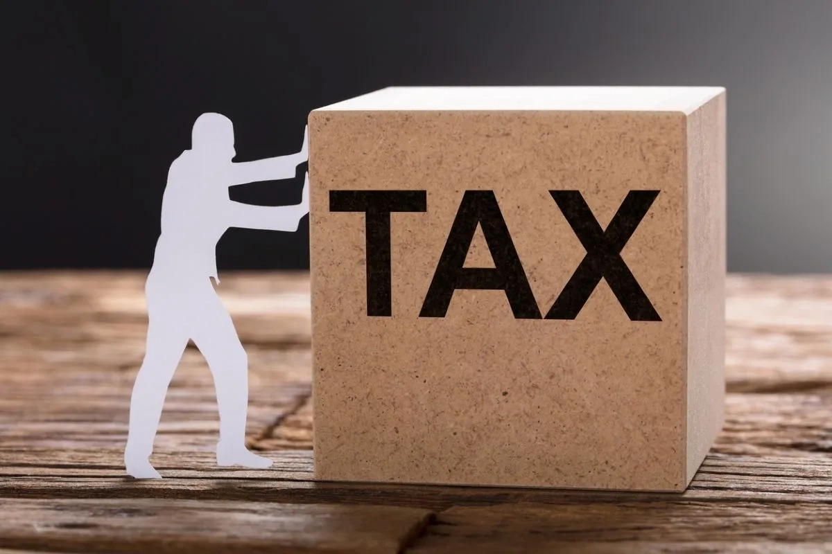 Closeup of paper man pushing tax wooden block on table against gray background
