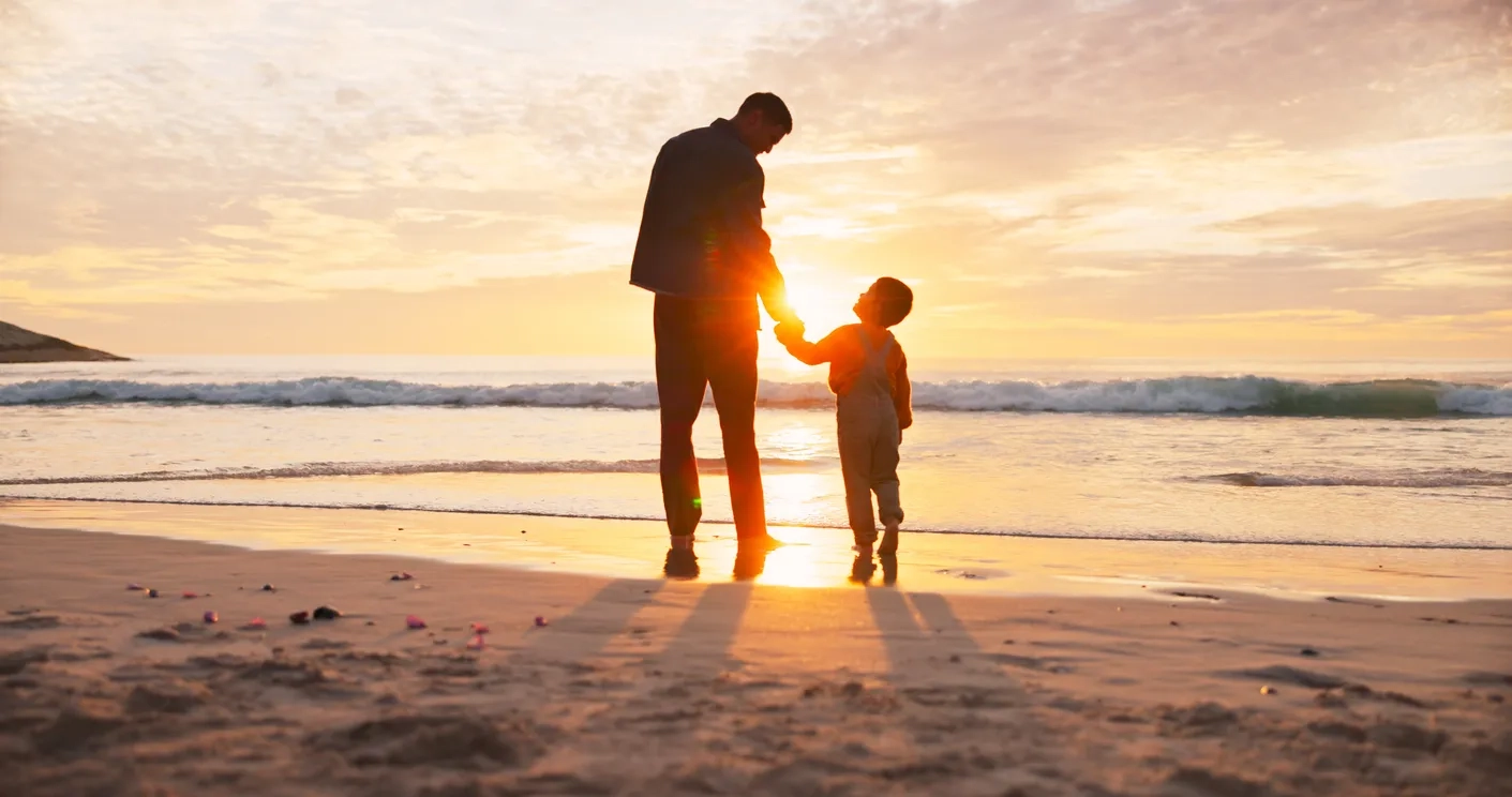 Man, child and holding hands at beach in summer for relax, travel and vacation as silhouette on sand. Family, back and walking at ocean with solidarity for holiday, trust and love together by sunset