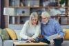 senior couple sitting on sofa looking at paper and electronic documents. Looking concerned.