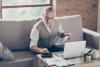 Old confident clever concentrated bearded grandpa is checking his calculations sitting in front of monitor at office