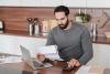 Busy concentrated Arabian man freelancer student counting calculating costs, expenses, income, rental taxes, doing paperwork in the kitchen using laptop.