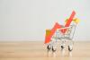 Shopping trolley with red chart falling down on wooden table background