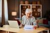 adult woman with short hair going through a financial report while sitting at a desk in front of a laptop and working from home