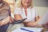 Old man and beautiful woman examining documents and using calculator while sitting on couch at home