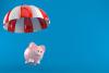 Piggy bank with parachute isolated on blue background