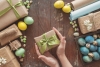 A young woman holds a gift in her hands in the background colored eggs on a dark wooden table. 