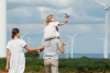 Family teaching young child about renewable energy and sustainability near wind turbines.