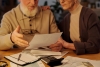 Financial bill in hands of senior man with beard sitting next to his wife during discussion of housing payment documents