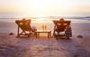 Couple relaxing on reclining chairs on the beach, in front of a sunset